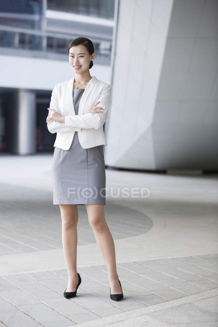 Chinese businesswoman standing in front of office building with arms folded — Stock Photo