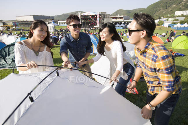Chinese friends setting up tent on grass — Stock Photo