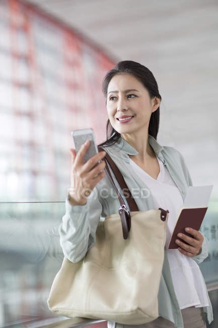 Mujer china sosteniendo teléfono inteligente y billete en el aeropuerto - foto de stock