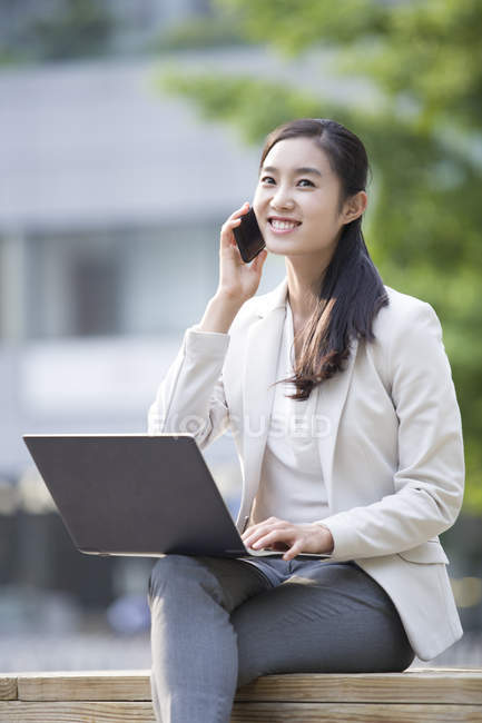 Chinese businesswoman talking on phone with laptop — Stock Photo