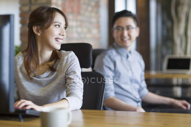 Китайський його робітники сидять і посміхаючись в офісі — стокове фото