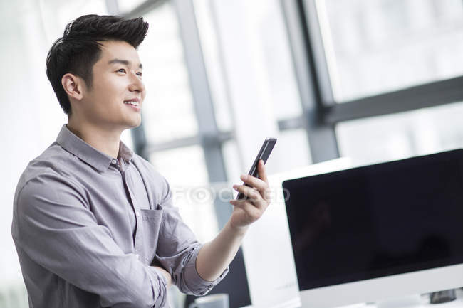Chinese businessman holding smartphone in office — Stock Photo