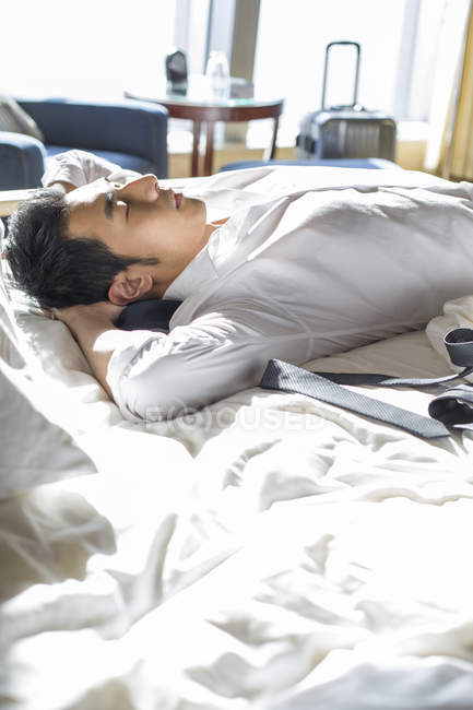Chinesischer Geschäftsmann ruht sich auf Bett im Hotelzimmer aus — Stockfoto