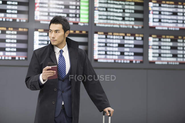 Китайський бізнесмен очікування в аеропорту з паспорт і смартфонів — стокове фото