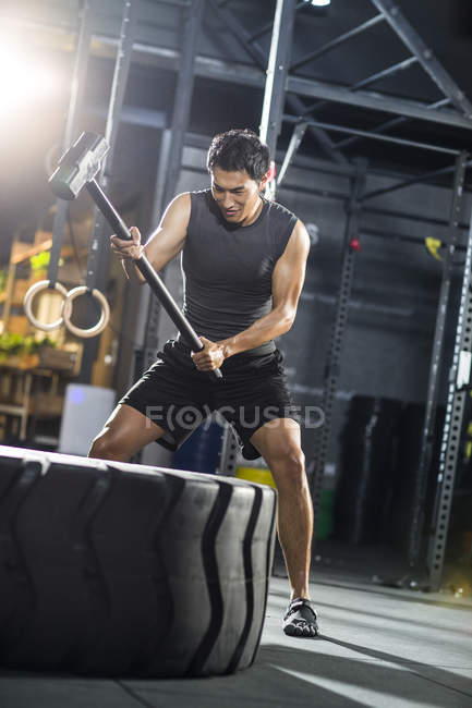 Homem chinês martelando pneu grande no ginásio — Fotografia de Stock