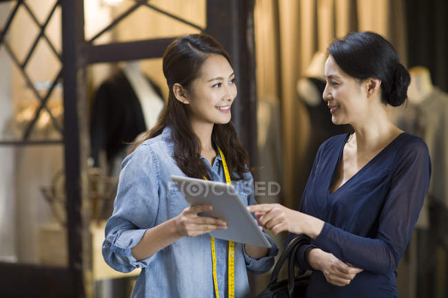 Chinese fashion designer and customer using digital tablet in atelier — Stock Photo