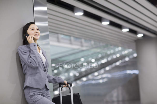 Donna d'affari cinese appoggiata al muro e che parla al telefono in aeroporto — Foto stock
