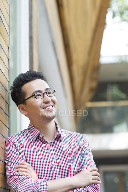 Homem chinês inclinado na parede e sorrindo — Fotografia de Stock
