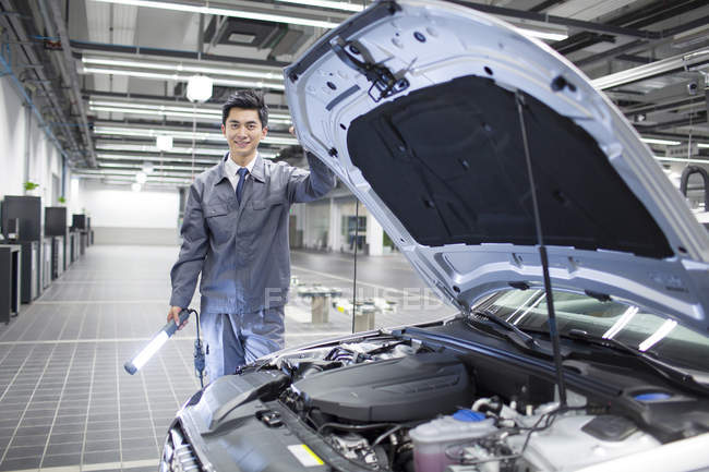 Mécanicien automobile chinois debout avec lampe de poche dans l'atelier — Photo de stock