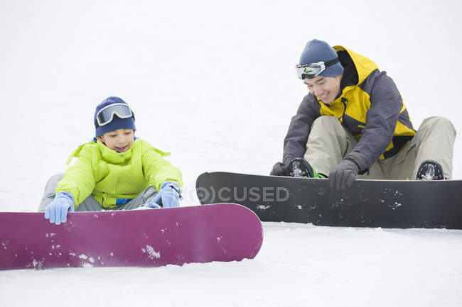 Chinese father and son sitting with snowboards on snow — Stock Photo