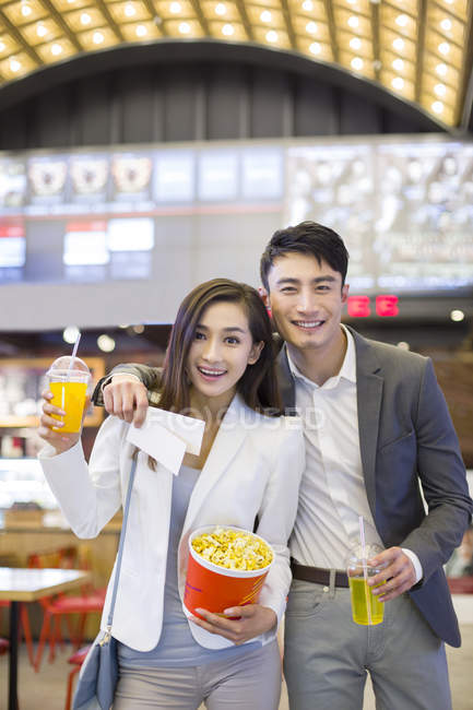 Chinese couple standing with popcorn and drinks in movie theater — Stock Photo