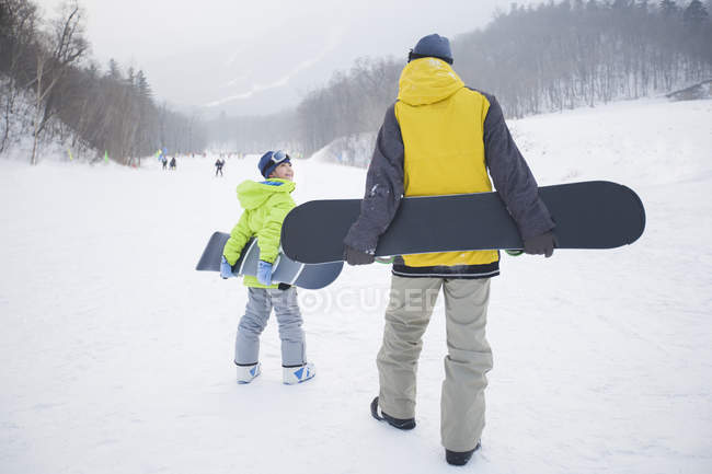 Padre e hijo caminando con tablas de snowboard sobre nieve - foto de stock