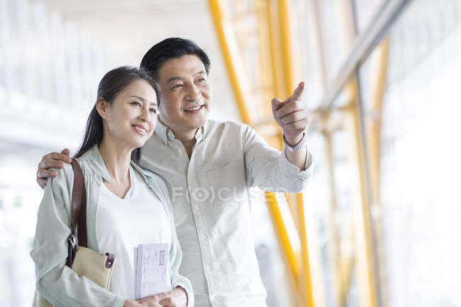 Mature chinese couple waiting and pointing at airport — Stock Photo