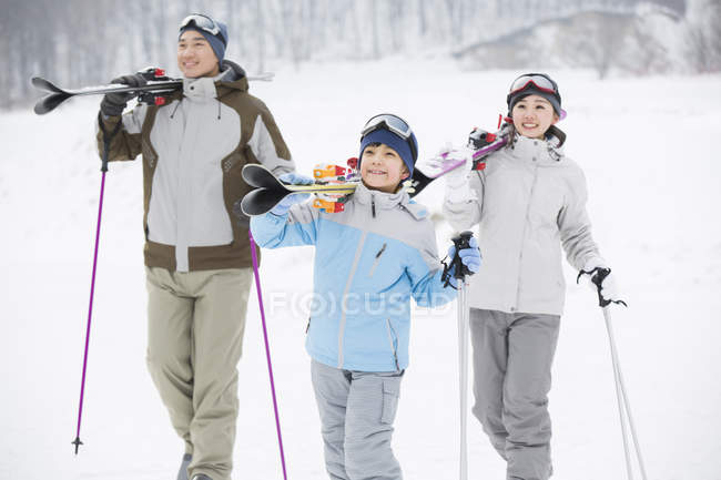 Chinese parents with son carrying skis on shoulders in ski resort — Stock Photo