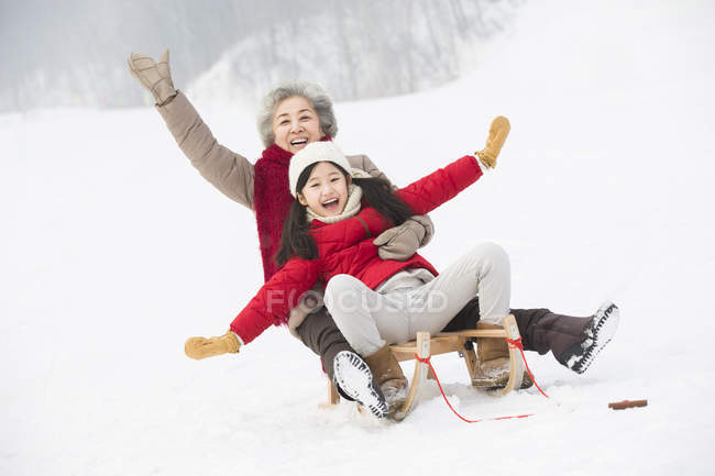 Chinese grandmother and granddaughter sliding on sled — Stock Photo