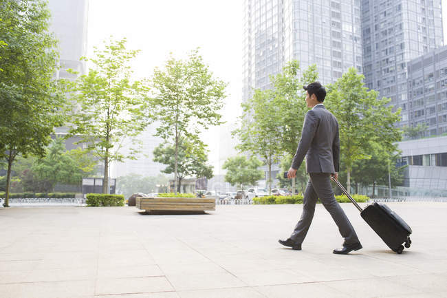 Chinese businessman walking and pulling suitcase on street — Stock Photo
