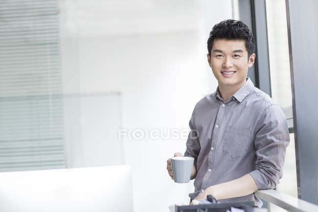 Homem de negócios chinês segurando xícara de café no escritório — Fotografia de Stock