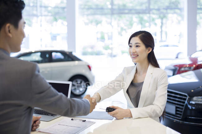 Chinese businesswoman making deal with car seller in showroom — Stock Photo