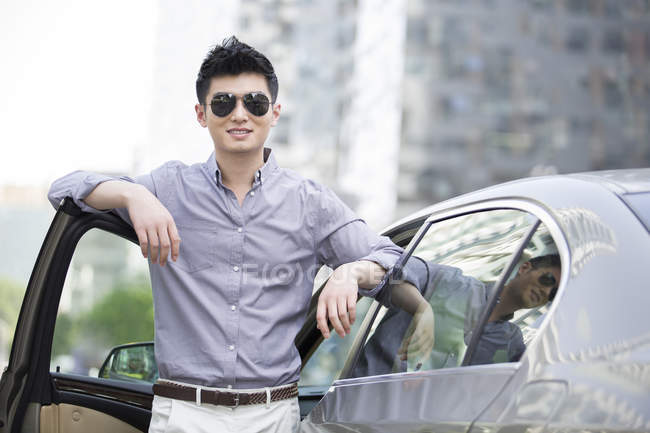 Chinese man in sunglasses standing at car open door — Stock Photo