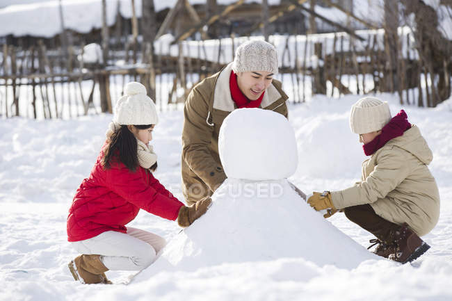 Chinese father and siblings making snowman together — Stock Photo