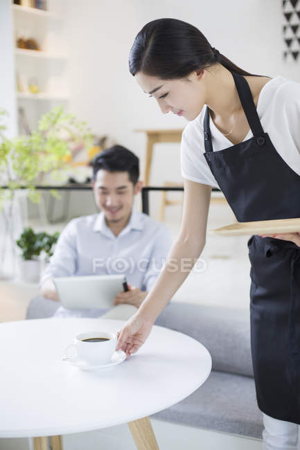 Chinese waitress serving man cup of coffee — Stock Photo