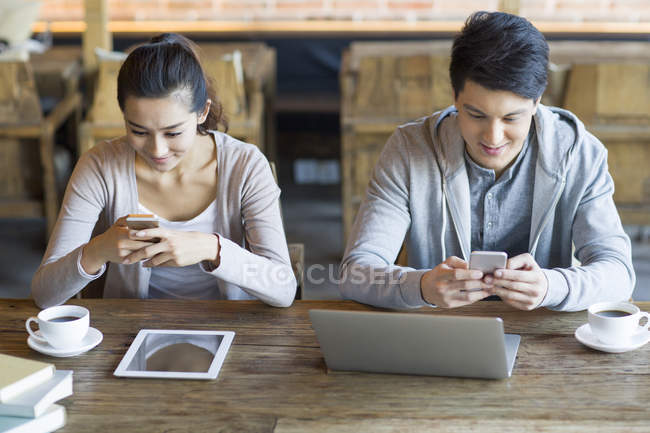 Chinese couple using smartphones in cafe — Stock Photo