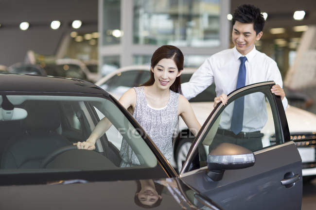 Chinese car seller helping woman getting in car in showroom — Stock Photo