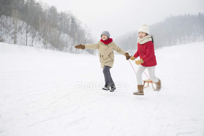 Chinese children running with sled in snowy park — Stock Photo