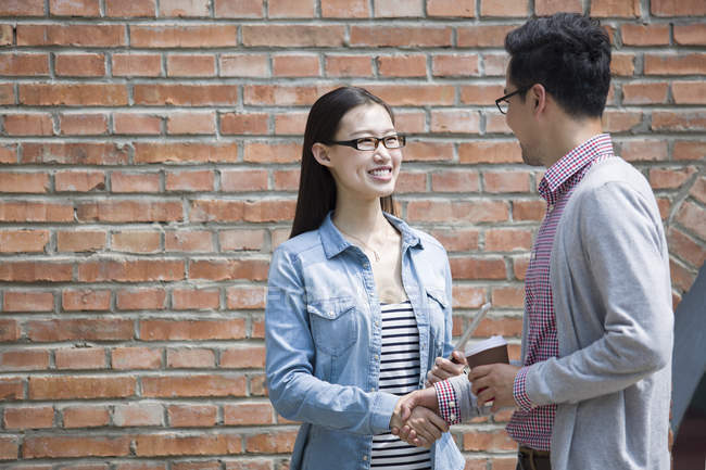 Chinese colleagues shaking hands in front of brick wall — Stock Photo