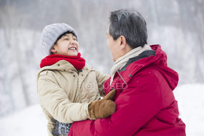 Abuelo y nieto chino abrazándose en la nieve - foto de stock