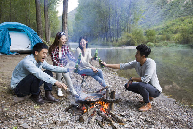 Chinese friends sitting around campfire with beer — Stock Photo
