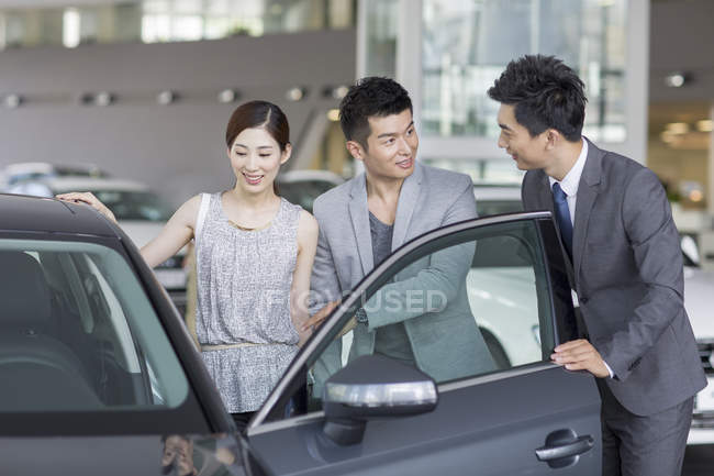 Chinese car dealer helping couple choosing car in showroom — Stock Photo