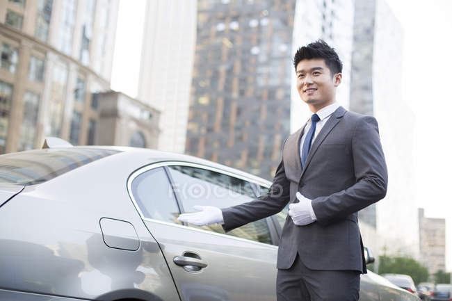 Chinese chauffeur making welcoming gesture at car — Stock Photo