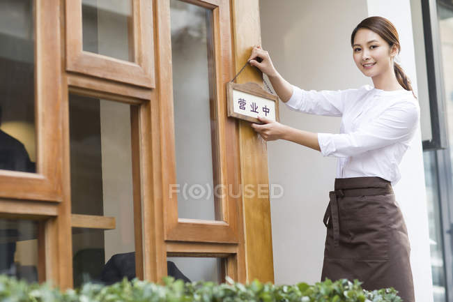 Cartel abierto de una joven camarera china colgando en la puerta del restaurante - foto de stock