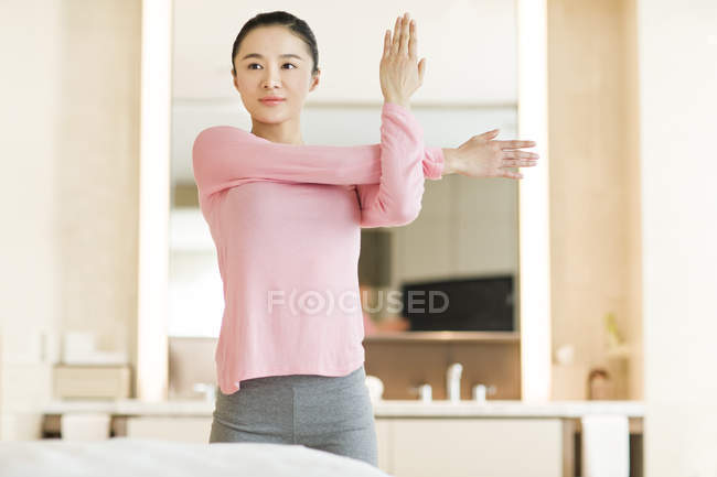 Donna cinese in abbigliamento sportivo rosa che si estende in camera da letto — Foto stock