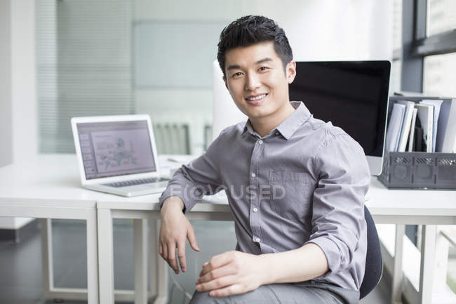 Hombre de negocios chino sentado en la silla en la oficina - foto de stock