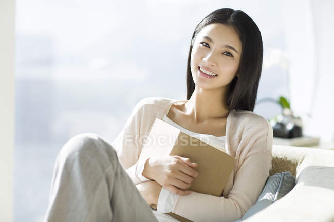 Chinese woman sitting on sofa with book — Stock Photo