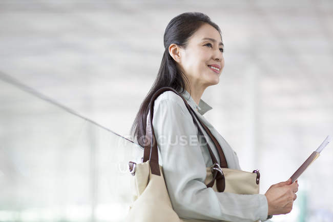 Mulher chinesa madura esperando no aeroporto com bilhete — Fotografia de Stock