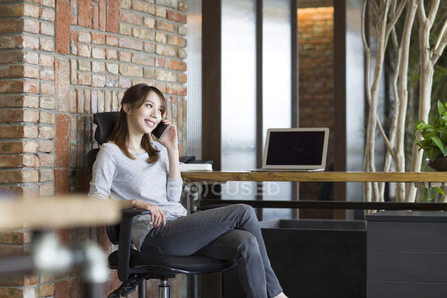 Chinese woman talking on phone in office chair — Stock Photo