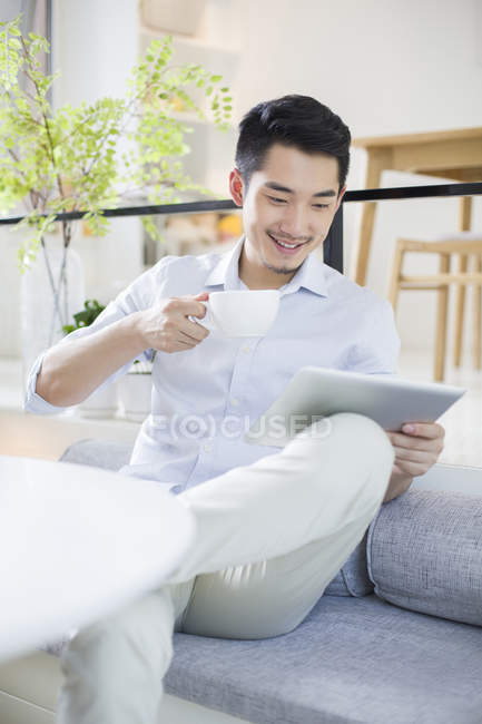 Chinese man holding digital tablet and coffee cup — Stock Photo