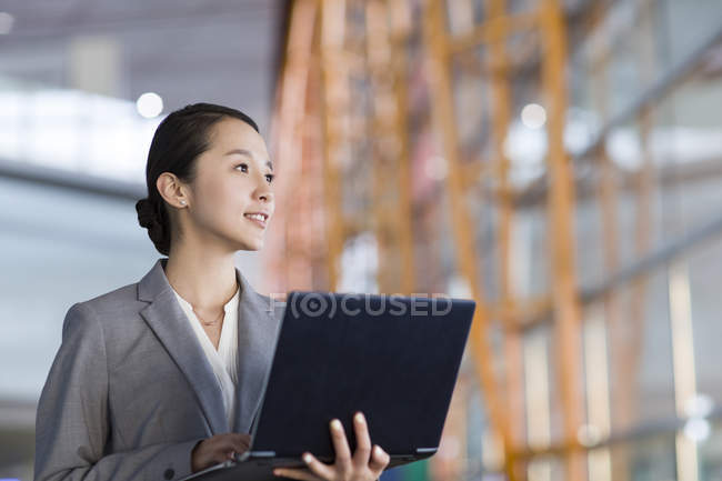 Chinesische Geschäftsfrau steht mit Laptop drinnen — Stockfoto