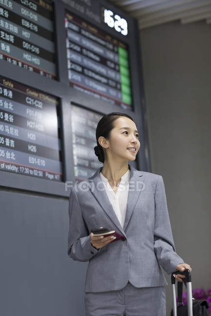 Chinese businesswoman holding passport and smartphone in airport — Stock Photo