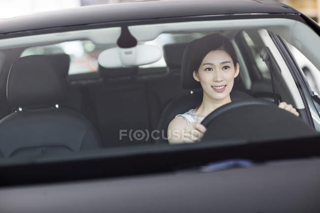Mujer china sentada en el coche y sosteniendo el volante - foto de stock