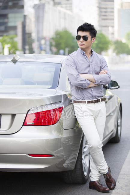 Chinese man leaning on car with arms folded — Stock Photo