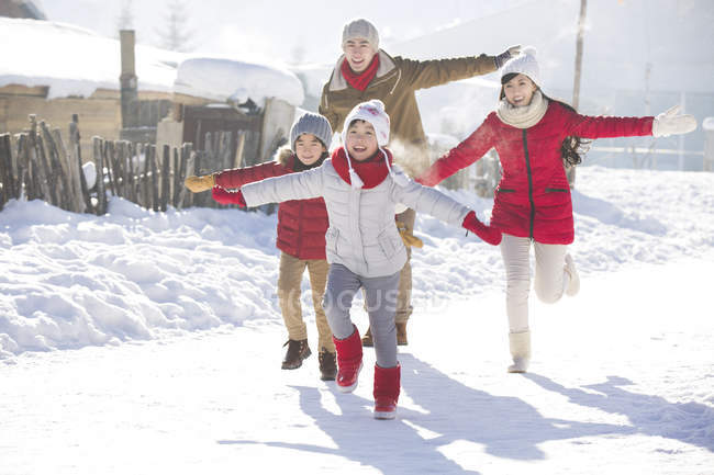 Família chinesa correndo na neve com os braços estendidos — Fotografia de Stock