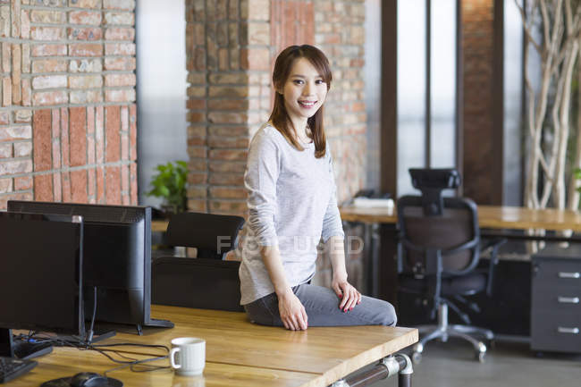 Китаянка, сидящая на столе в офисе — стоковое фото