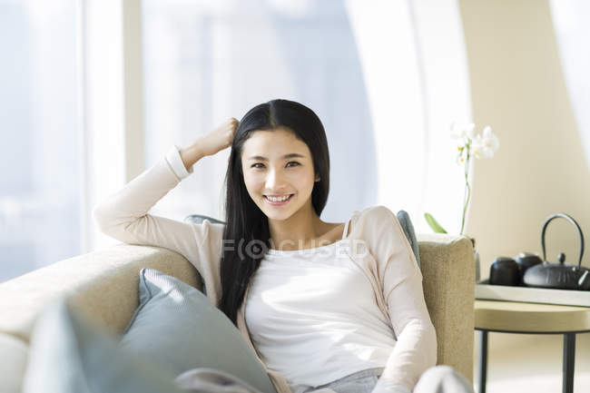 Китаянка, опирающаяся на диван и смотрящая в камеру — стоковое фото