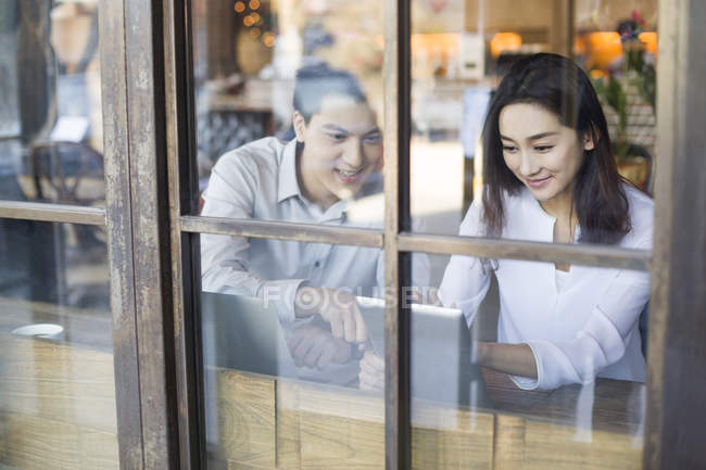 Chinese man and woman using digital tablet behind cafe window — Stock Photo