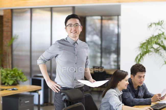 Chino trabajador de TI masculino de pie con papeles en la oficina - foto de stock