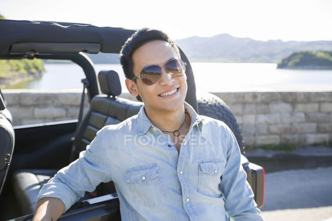 Chinese man leaning on car in suburbs — Stock Photo